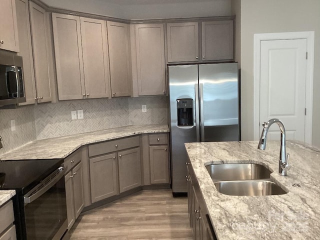 kitchen with light stone countertops, tasteful backsplash, stainless steel appliances, sink, and light hardwood / wood-style floors