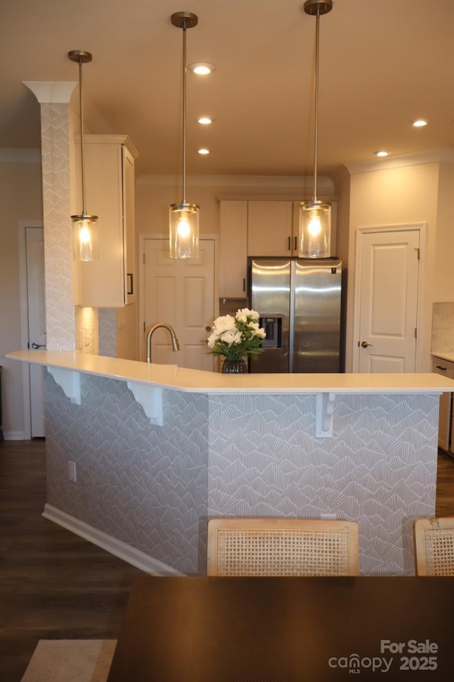 kitchen with stainless steel fridge, dark wood-type flooring, light countertops, white cabinetry, and pendant lighting