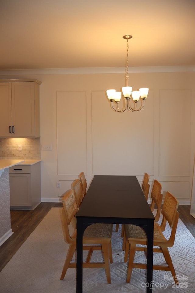 dining room with ornamental molding, dark wood-type flooring, a decorative wall, and an inviting chandelier