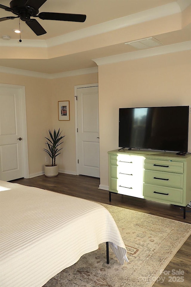 bedroom with ornamental molding, dark wood-type flooring, a raised ceiling, and baseboards