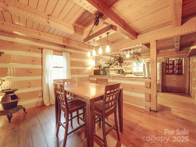 dining space with beamed ceiling, wooden walls, wooden ceiling, and light wood-type flooring