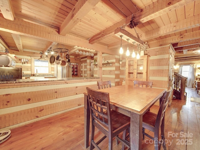 dining area featuring light hardwood / wood-style flooring, wooden ceiling, beamed ceiling, and wood walls