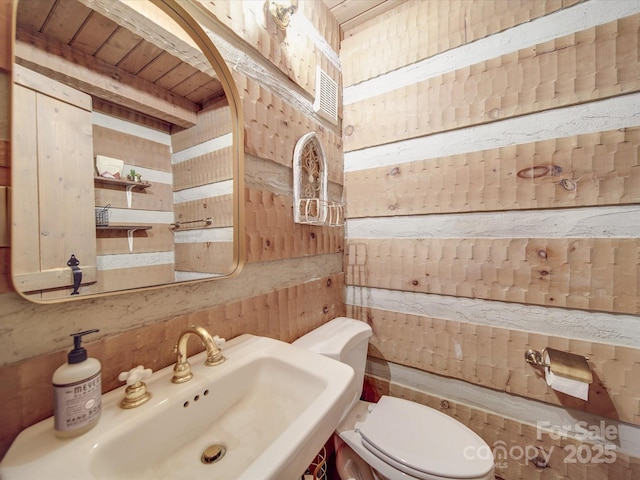 bathroom featuring toilet, sink, and wood walls