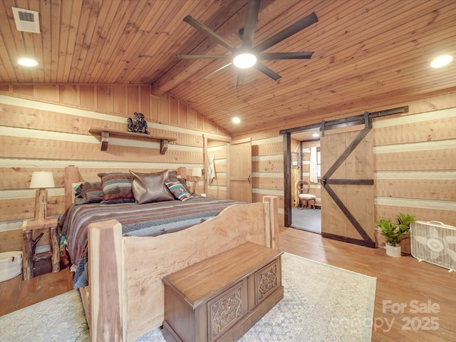 bedroom with lofted ceiling, light wood-type flooring, wooden ceiling, wooden walls, and a barn door