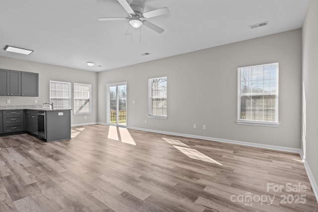 unfurnished living room featuring ceiling fan, light wood-type flooring, sink, and a wealth of natural light