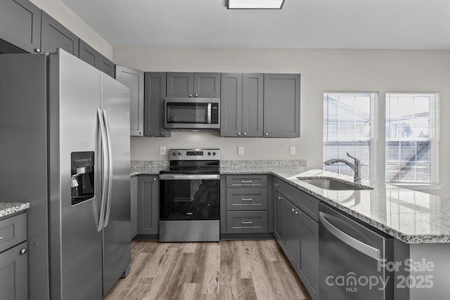 kitchen with kitchen peninsula, appliances with stainless steel finishes, light wood-type flooring, gray cabinetry, and sink