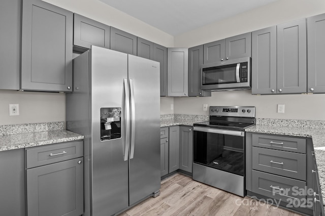 kitchen featuring stainless steel appliances, gray cabinets, light hardwood / wood-style floors, and light stone counters