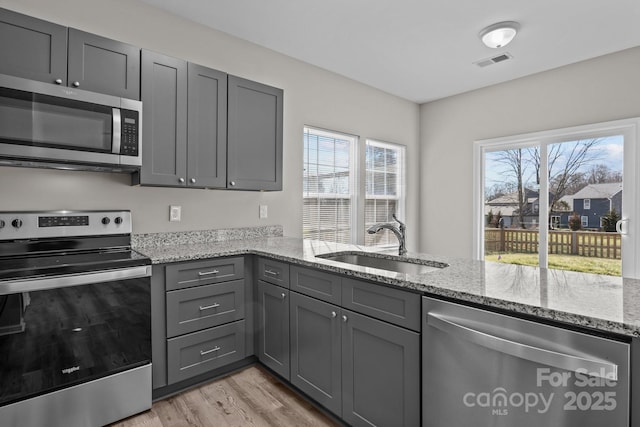 kitchen with light stone countertops, sink, stainless steel appliances, kitchen peninsula, and gray cabinets