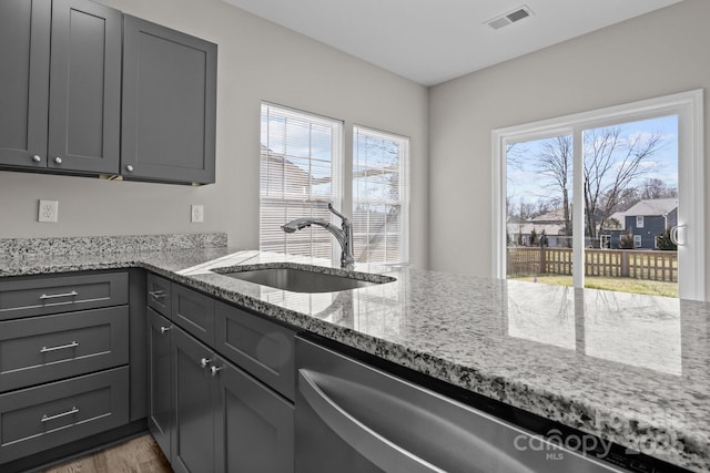 kitchen featuring sink, dishwasher, light stone counters, gray cabinets, and hardwood / wood-style flooring