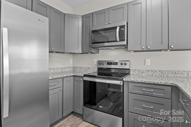 kitchen featuring gray cabinetry, light stone countertops, appliances with stainless steel finishes, and light hardwood / wood-style flooring