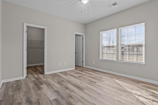 unfurnished bedroom with a closet, a spacious closet, ceiling fan, and light hardwood / wood-style flooring