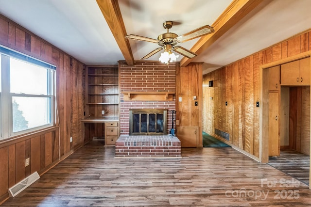 unfurnished living room with a brick fireplace, built in shelves, ceiling fan, and wood walls