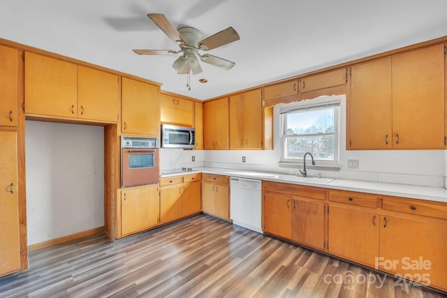 kitchen with sink, ceiling fan, wall oven, white dishwasher, and wood-type flooring