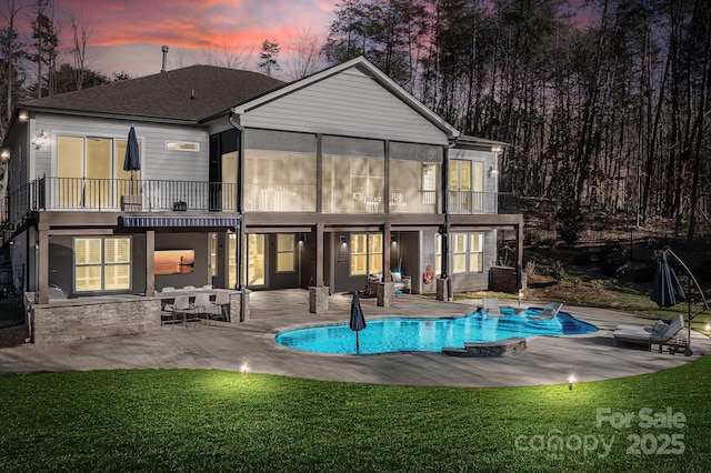 back house at dusk featuring a sunroom, a yard, and a patio