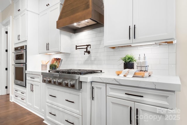 kitchen featuring decorative backsplash, custom range hood, appliances with stainless steel finishes, light stone counters, and white cabinetry