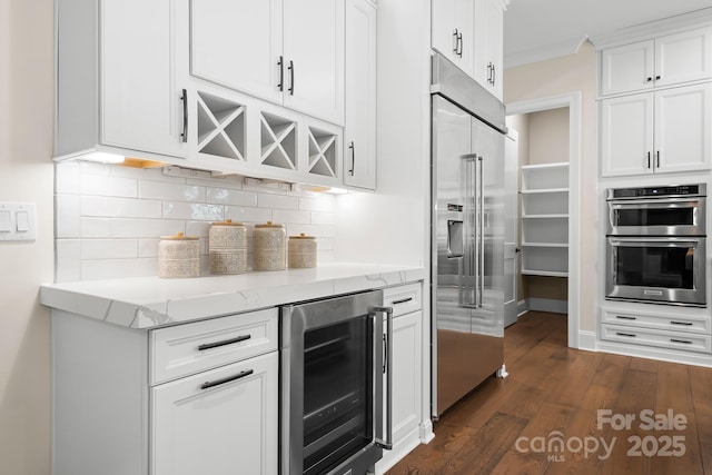 kitchen featuring white cabinets, light stone counters, appliances with stainless steel finishes, dark hardwood / wood-style flooring, and beverage cooler