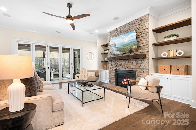 living room with built in shelves, hardwood / wood-style flooring, a stone fireplace, and ceiling fan