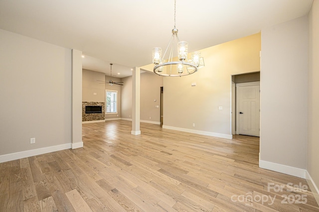 interior space featuring ceiling fan with notable chandelier, a stone fireplace, and light wood-type flooring