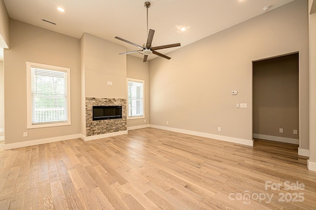 unfurnished living room featuring ceiling fan, a stone fireplace, light wood-type flooring, and a wealth of natural light