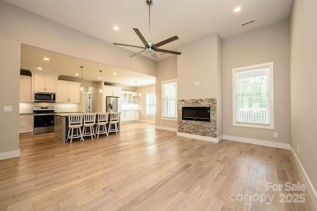 living room with light wood-type flooring, a stone fireplace, and ceiling fan