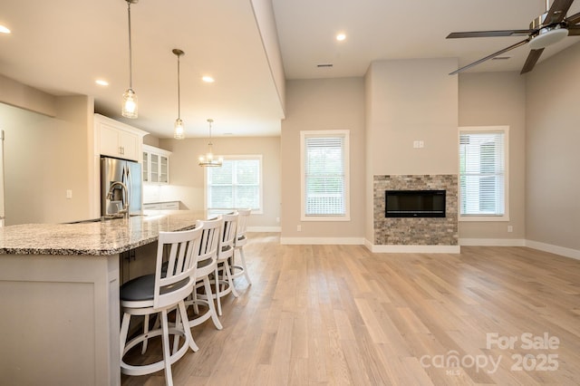 kitchen featuring hanging light fixtures, a stone fireplace, a spacious island, white cabinets, and ceiling fan with notable chandelier