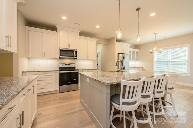 kitchen featuring a center island with sink, pendant lighting, white cabinetry, and stainless steel appliances