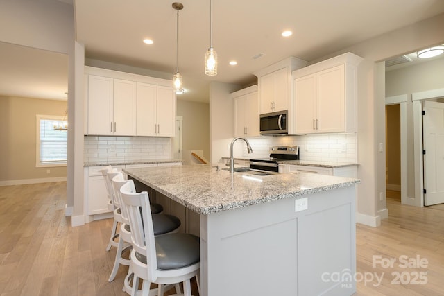 kitchen featuring white cabinetry, light stone counters, pendant lighting, a center island with sink, and appliances with stainless steel finishes