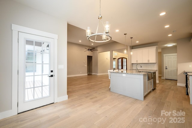 kitchen with sink, hanging light fixtures, a center island with sink, white cabinets, and ceiling fan with notable chandelier