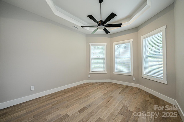 spare room with light wood-type flooring, a tray ceiling, and ceiling fan