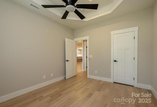 unfurnished bedroom with a tray ceiling, light hardwood / wood-style flooring, and ceiling fan