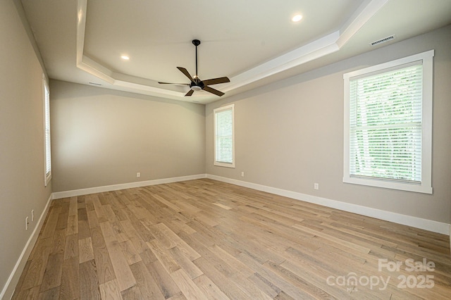 unfurnished room with a raised ceiling, ceiling fan, and light wood-type flooring