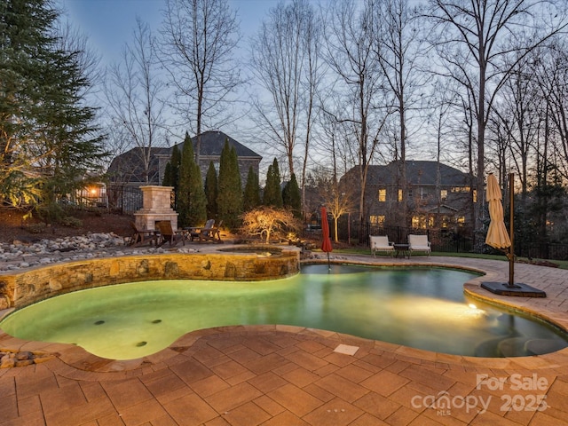 pool at dusk featuring a patio area and an outdoor fireplace