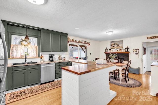 kitchen with a textured ceiling, pendant lighting, stainless steel dishwasher, and green cabinetry