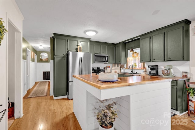 kitchen featuring light wood-type flooring, stainless steel appliances, green cabinetry, and sink