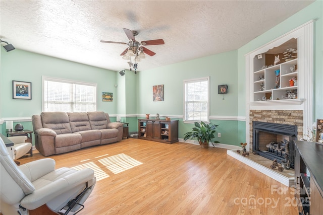 living room featuring a stone fireplace, ceiling fan, hardwood / wood-style floors, and a textured ceiling