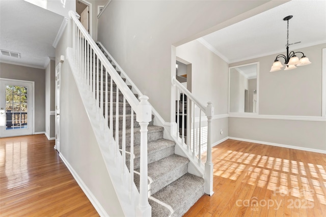 stairs with wood-type flooring, ornamental molding, and an inviting chandelier