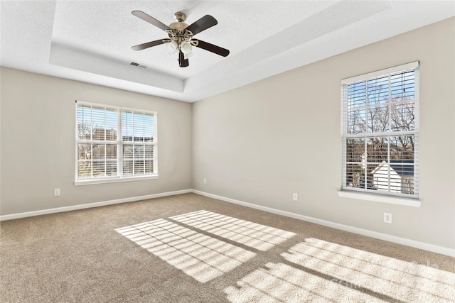 carpeted empty room with a textured ceiling, a tray ceiling, ceiling fan, and a healthy amount of sunlight