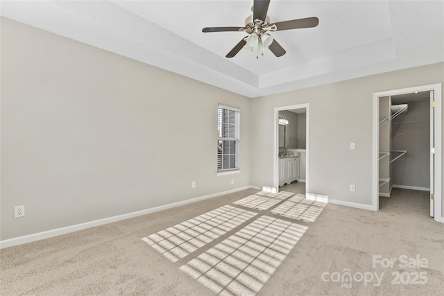 unfurnished bedroom with a raised ceiling, a walk in closet, ceiling fan, and a closet