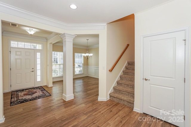 foyer with decorative columns, wood-type flooring, ornamental molding, and an inviting chandelier