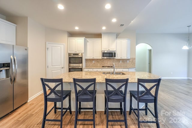 kitchen featuring sink, stainless steel appliances, a kitchen island with sink, and light stone countertops