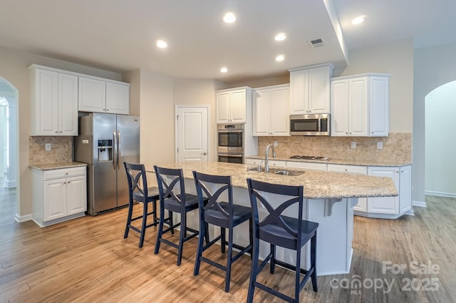 kitchen with appliances with stainless steel finishes, white cabinets, sink, light stone counters, and a center island with sink