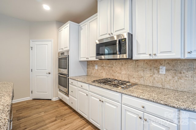 kitchen featuring light hardwood / wood-style flooring, backsplash, white cabinets, light stone countertops, and stainless steel appliances