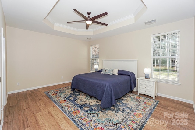 bedroom with ceiling fan, hardwood / wood-style flooring, a tray ceiling, and ornamental molding