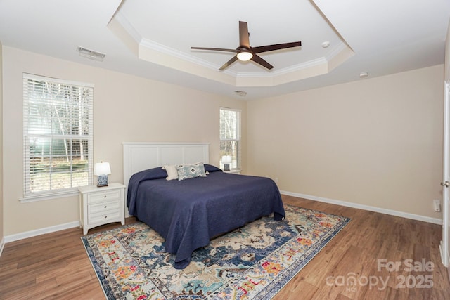 bedroom with ceiling fan, a raised ceiling, ornamental molding, and hardwood / wood-style flooring