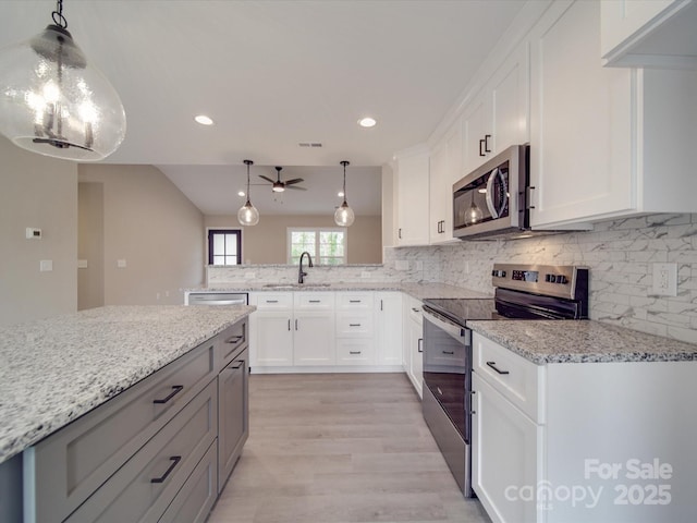 kitchen featuring stainless steel appliances, a peninsula, a sink, backsplash, and light stone countertops