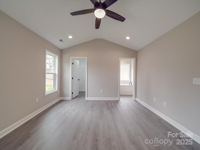 unfurnished bedroom featuring baseboards, visible vents, wood finished floors, a walk in closet, and vaulted ceiling