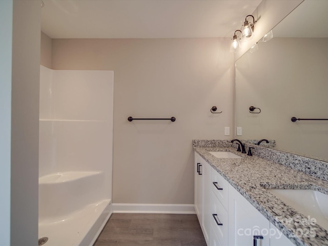 full bathroom with wood finished floors, walk in shower, a sink, and baseboards