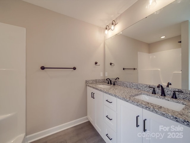 bathroom featuring double vanity, a sink, baseboards, and wood finished floors