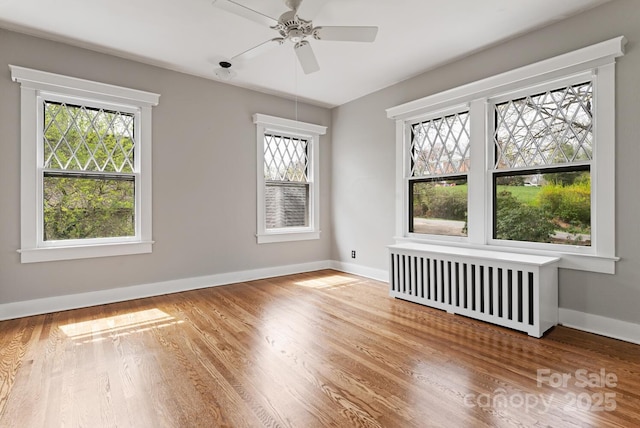 spare room with hardwood / wood-style flooring, plenty of natural light, ceiling fan, and radiator heating unit