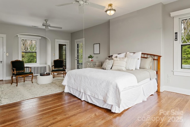 bedroom featuring multiple windows, ceiling fan, wood-type flooring, and radiator